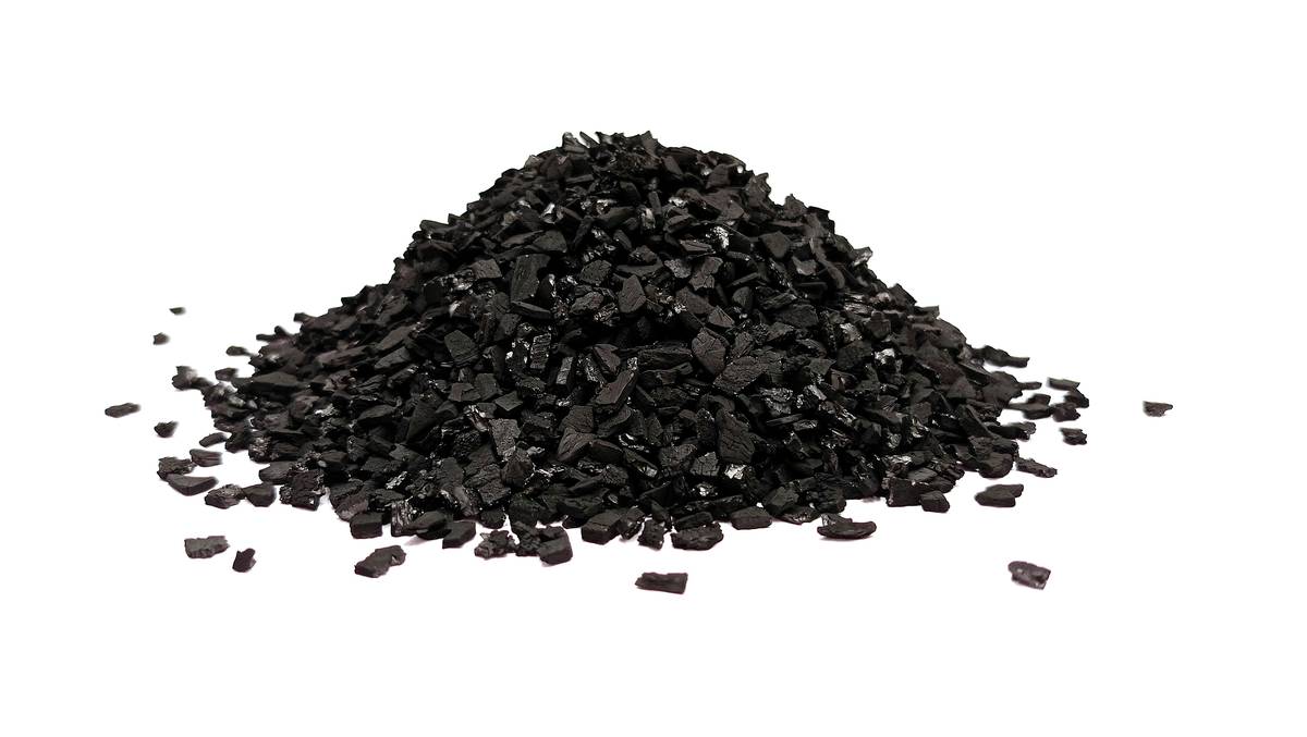 Hand spreading granular humate soil conditioner over garden bed with trowel